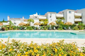 A poolside view of a resort with white buildings, palm trees, and a clear blue sky. - Jardins do Golfe Top Floor Retreat (Vale do Lobo)