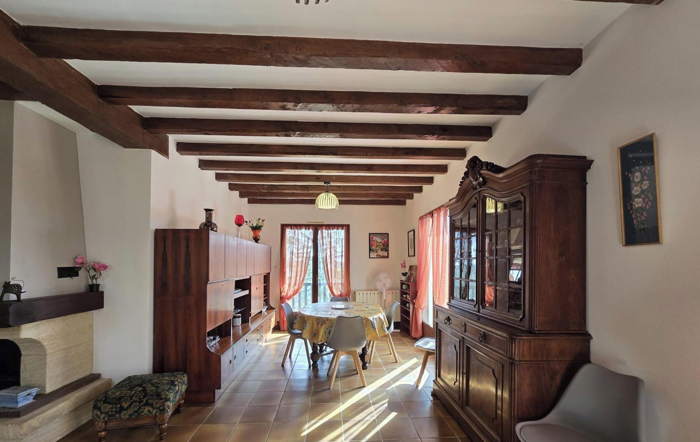 Amplia sala de estar con techo alto, vigas de madera a la vista, chimenea, comedor con mesa y sillas, y un gran aparador de madera.