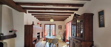 Amplia sala de estar con techo alto, vigas de madera a la vista, chimenea, comedor con mesa y sillas, y un gran aparador de madera.