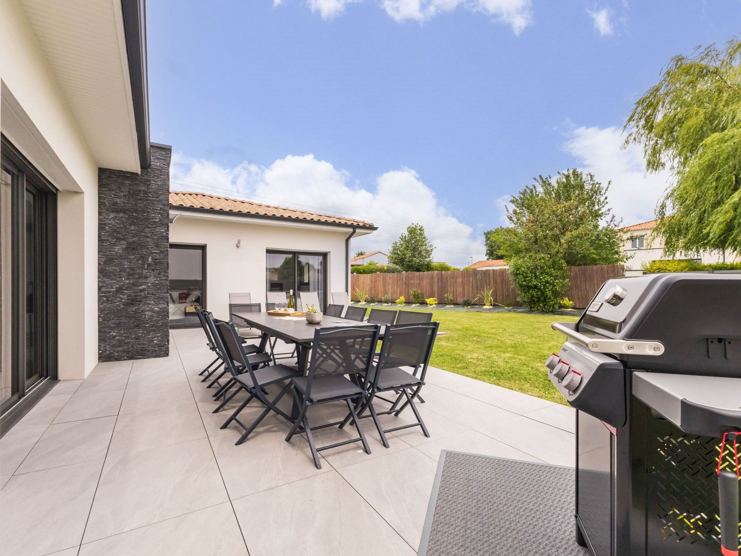 Un patio al aire libre con mesa y sillas, una parrilla y una casa al fondo.