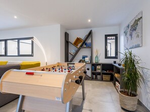 Ett modernt vardagsrum med ett fotbollsspel, en soffa med gula kuddar, en bokhylla och en stor världskarta på väggen.