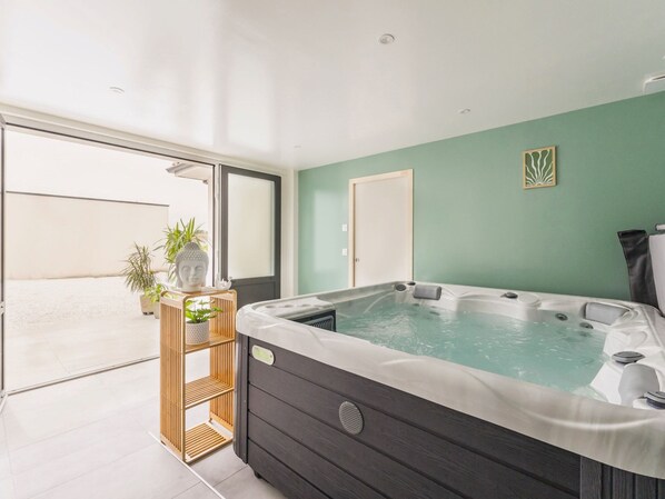 Un baño moderno con una bañera grande, un estante de madera con plantas y una pared verde.