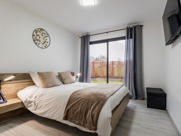 A bedroom with a bed, bedside table, lamp, and a large window with curtains.