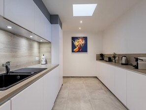 A modern kitchen with a black sink, white cabinets, and a skylight.
