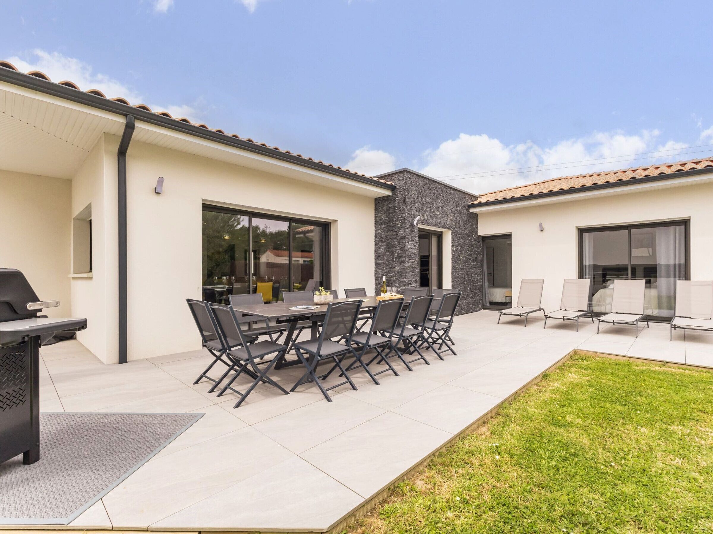 A patio with a dining table and chairs, a grill, and a small garden area.