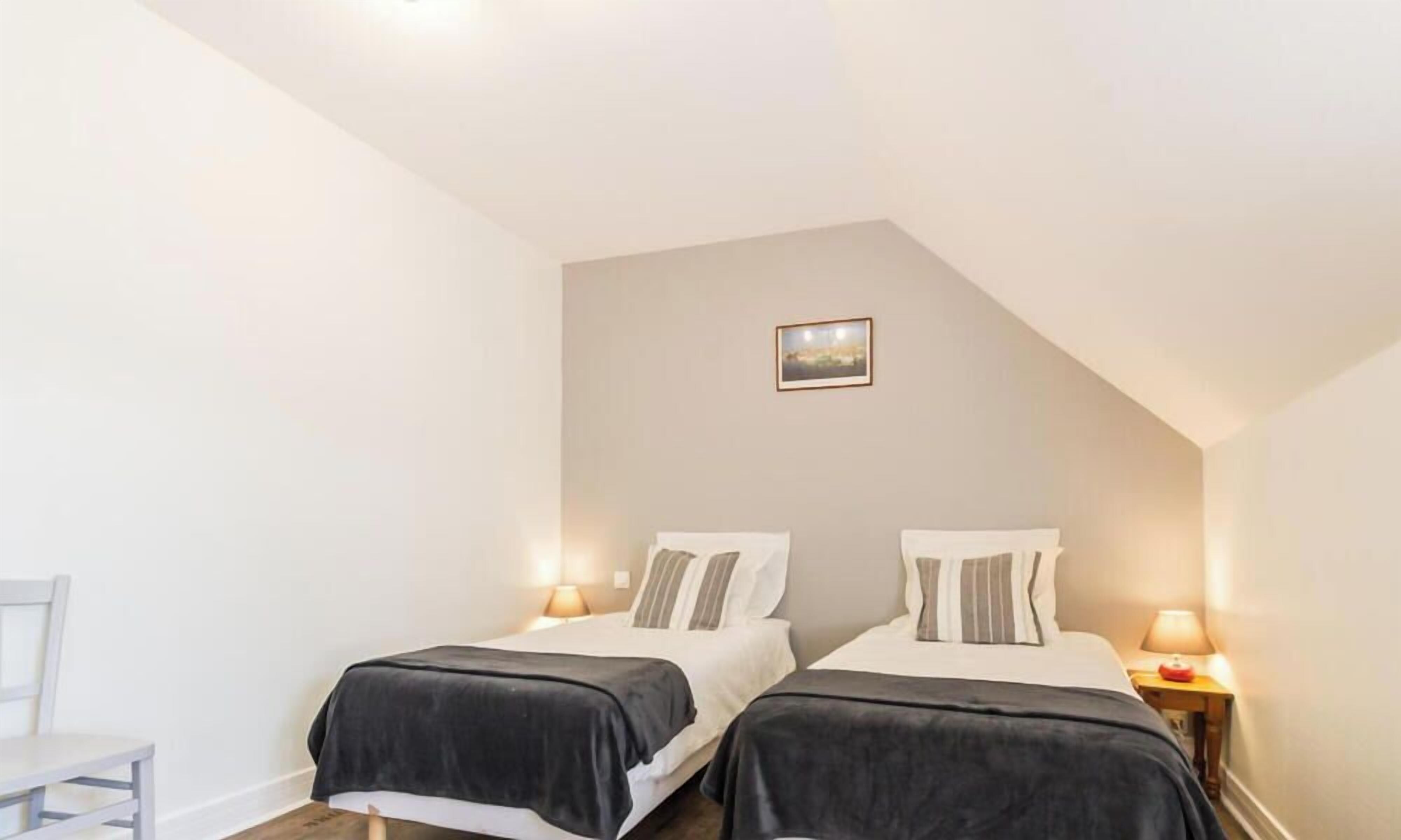 A bedroom with two beds, each with a pillow and a bedside table with a lamp.