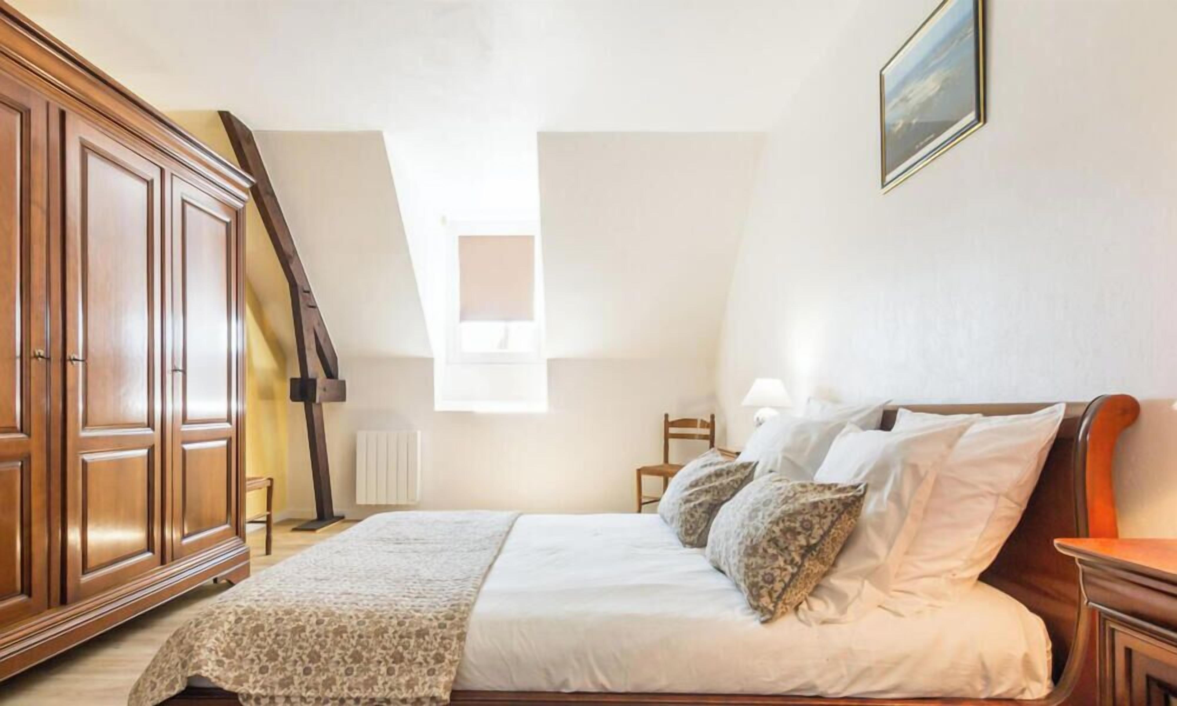 Un dormitorio con una cama grande, armario de madera y techo inclinado con tragaluz.