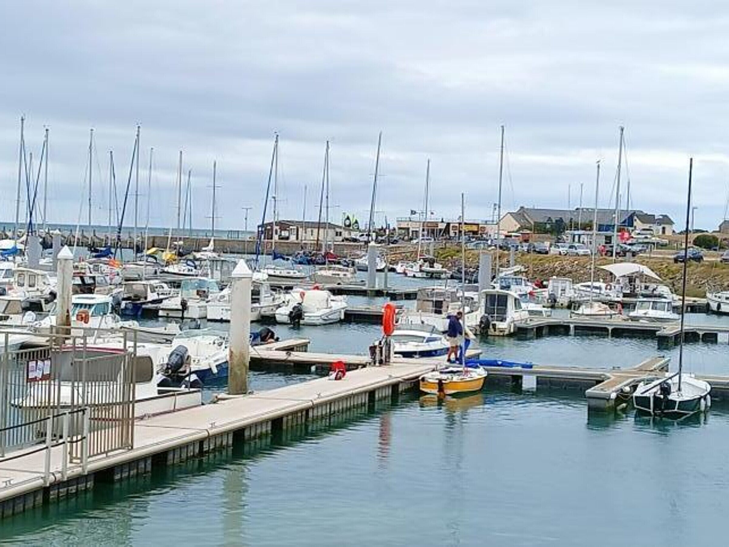 Un puerto deportivo con varias embarcaciones amarradas, un muelle y edificios al fondo.