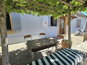 A wooden table and chairs under a pergola with grapevines, a white building with windows, and a potted plant. - Large cottage, parking, pets welcome - 10 guests (Bars)