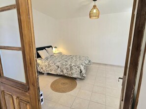 A bedroom with a bed, a bedside lamp, a woven rug, and a hanging light fixture. - Large cottage, parking, pets welcome - 10 guests (Bars)