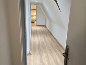 Un pasillo con suelo de madera y paredes blancas que conduce a una habitación con cama.