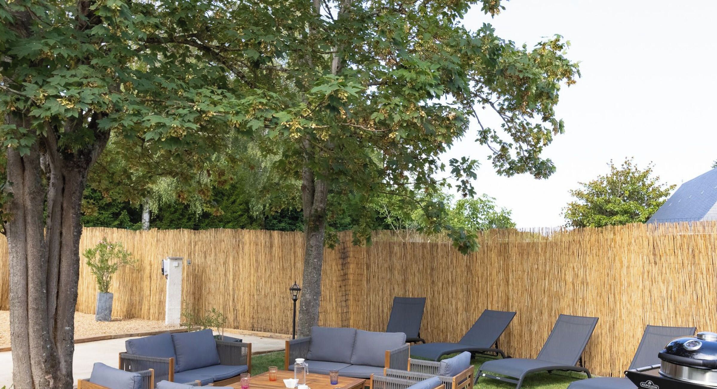 An outdoor seating area with lounge chairs and a table, surrounded by a bamboo fence and trees.