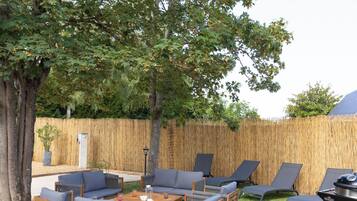 An outdoor seating area with lounge chairs and a table, surrounded by a bamboo fence and trees.