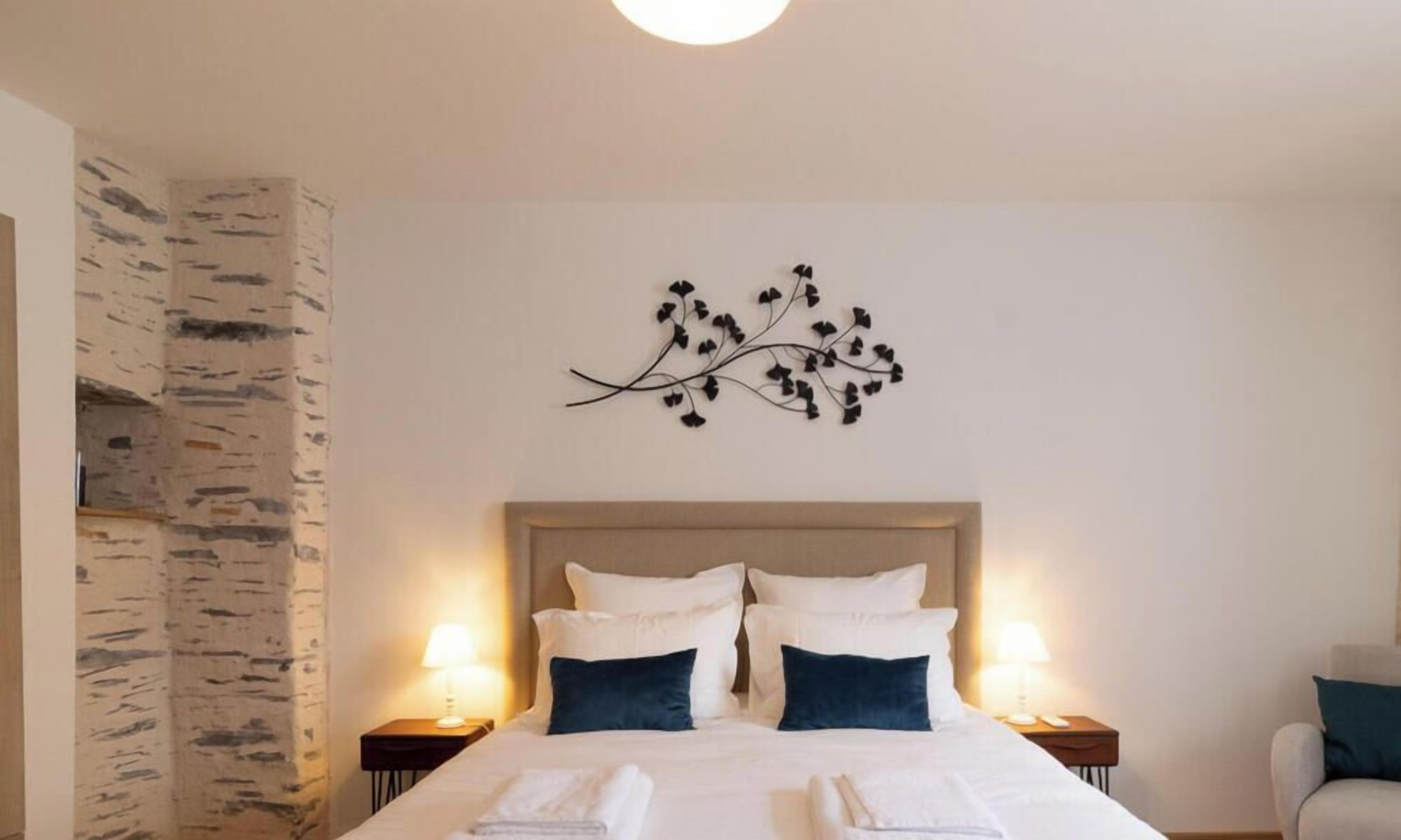 Habitación de hotel con cama, dos mesitas de noche, una decoración de ramas en la pared y pared texturizada en un lateral.