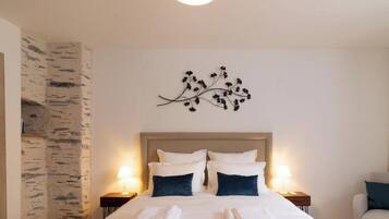 Habitación de hotel con cama, dos mesitas de noche, una decoración de ramas en la pared y pared texturizada en un lateral.