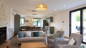 Una sala de estar moderna con un sofá, sillones y una mesa de centro. Se observa una cocina al fondo con un comedor.