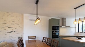 Una cocina moderna con comedor, que incluye una mesa y sillas de madera, horno empotrado e iluminación colgante.