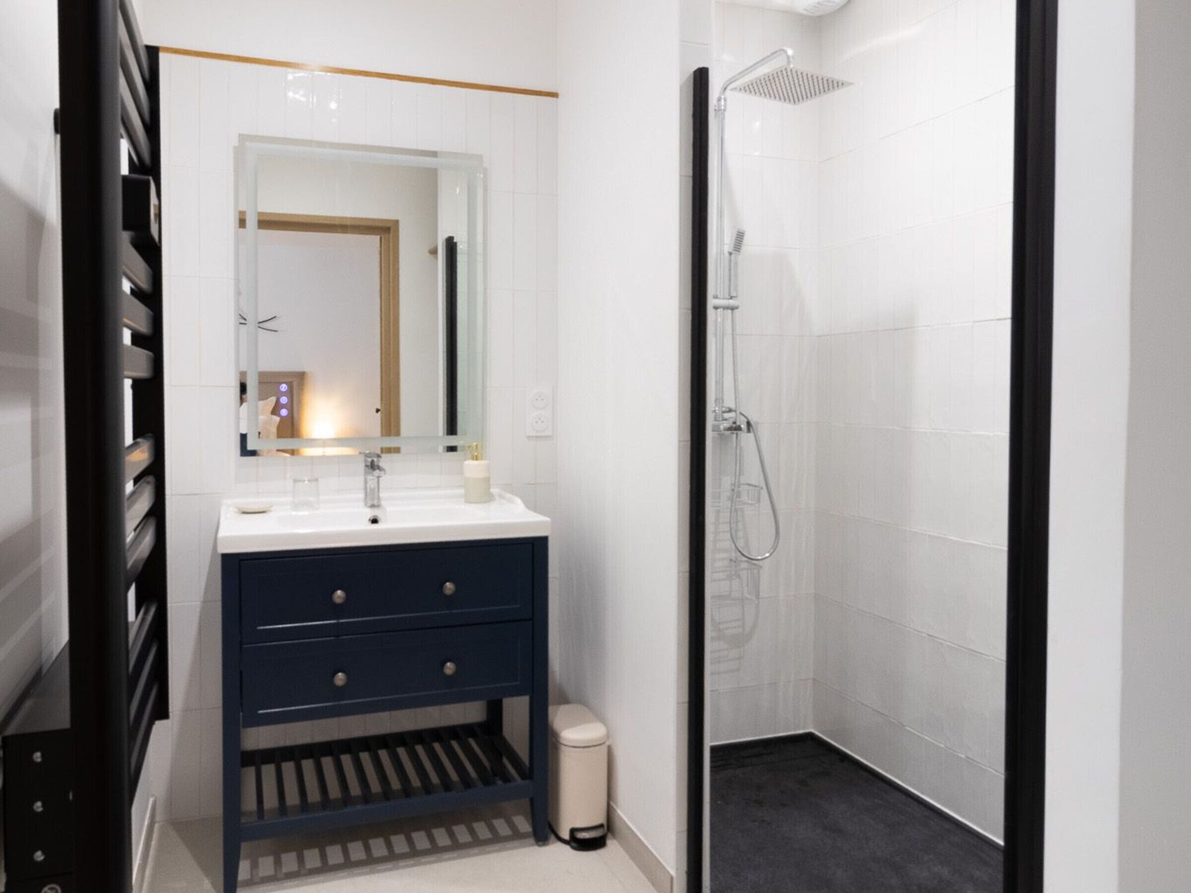 Ein modernes Badezimmer mit einem weißen Waschbecken, einer dunkelblauen Kommode und einer Duschkabine aus Glas.
