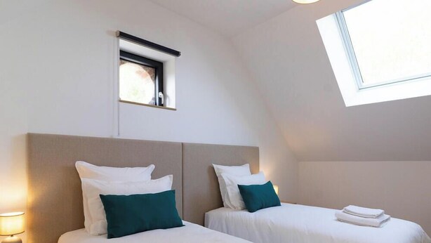Una habitación con dos camas, una ventana pequeña y una lámpara.