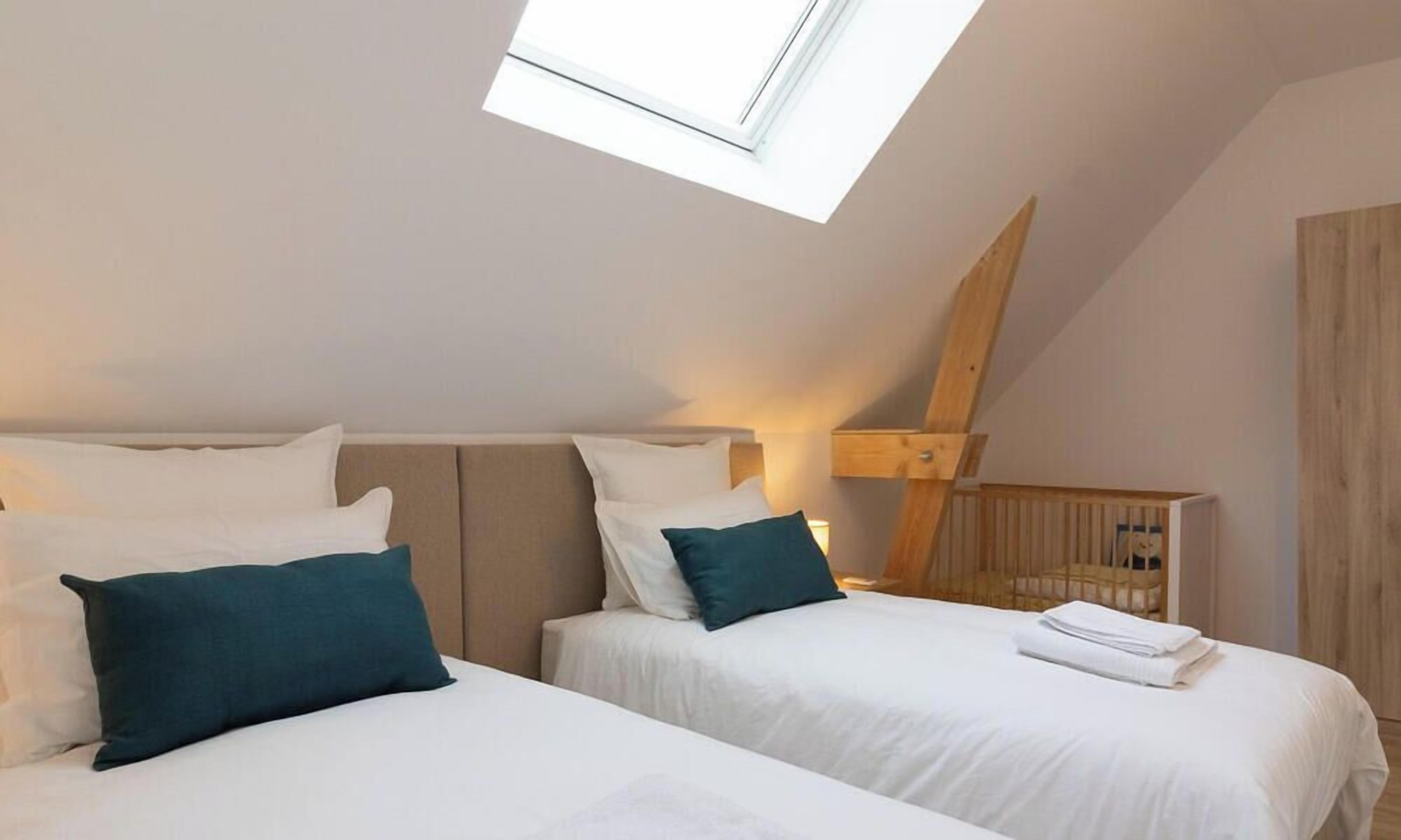 A bedroom with two beds, a skylight, and a crib.