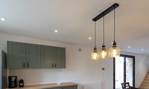 A kitchen with green cabinets, a wooden countertop, and pendant lighting.