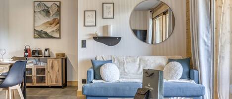 A modern living room with a blue sofa, a coffee table, and a dining area with a wooden cabinet.