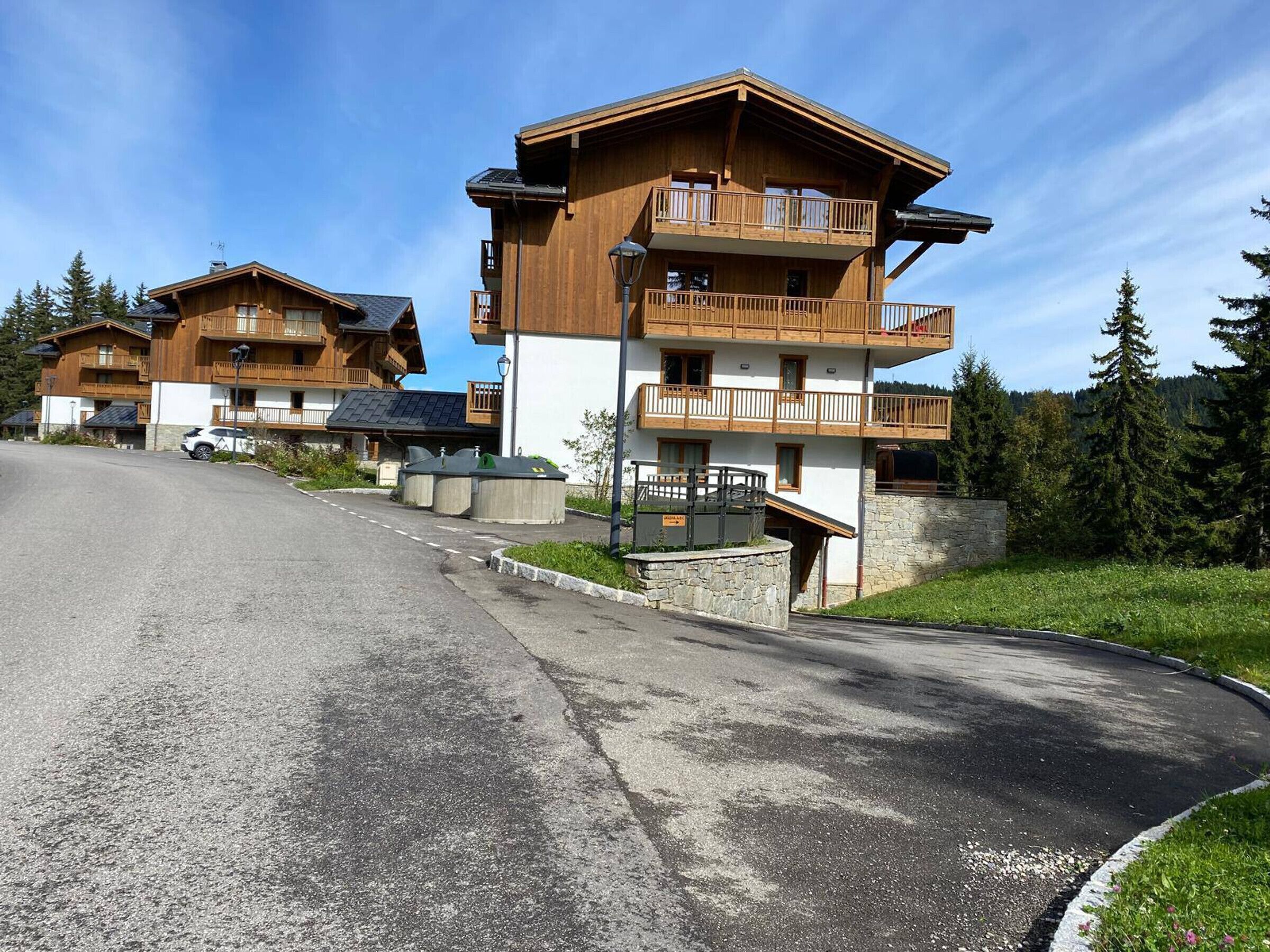 A row of wooden chalet-style buildings with balconies, a paved road, and a forested backdrop.