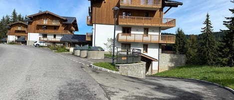 Une rangée de bâtiments de style chalet en bois, dotés de balcons, une route pavée et un paysage boisé en arrière-plan.