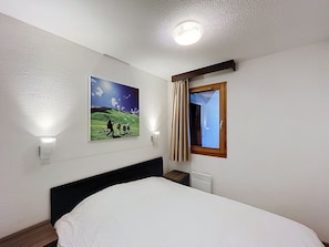 A hotel room with a bed, a wall-mounted picture, a window with curtains, and a ceiling light. - Bright apartment mountain view - 6 guests (Saint-Chaffrey)