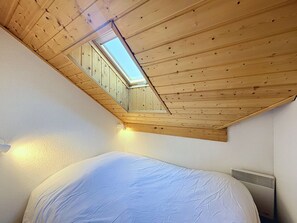 Une pièce avec un plafond en pente, un puits de lumière, un lit et un radiateur fixé au mur.