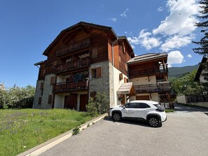 A multi-story wooden building with balconies, a stone facade, and a parked car. - Bright apartment mountain view - 6 guests (Saint-Chaffrey)
