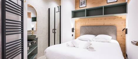 A modern bedroom with a bed, a built-in bench, a mirror, and a wooden ceiling.