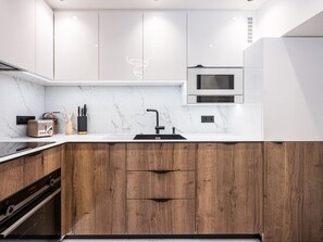 A modern kitchen with a marble countertop, wooden cabinets, a built-in oven, and a microwave. - Luxury apartment - 10 guests (Tignes)