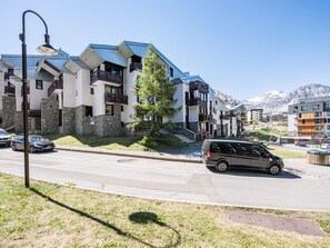 A modern multi-story building with balconies, a parking area, and a mountain backdrop. - Luxury apartment - 10 guests (Tignes)