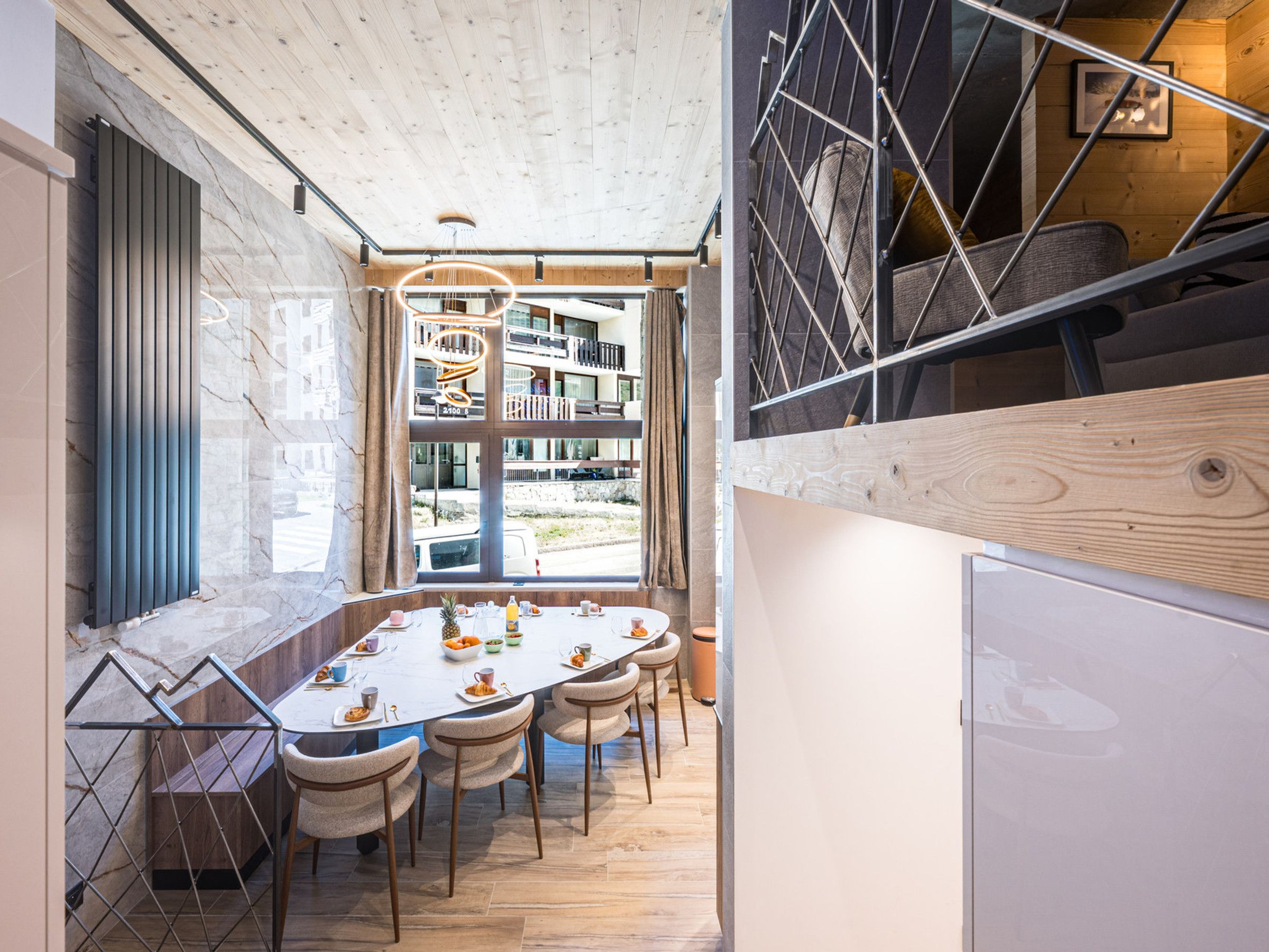 A modern dining area with a round table, chairs, and a view of the cityscape through large windows.