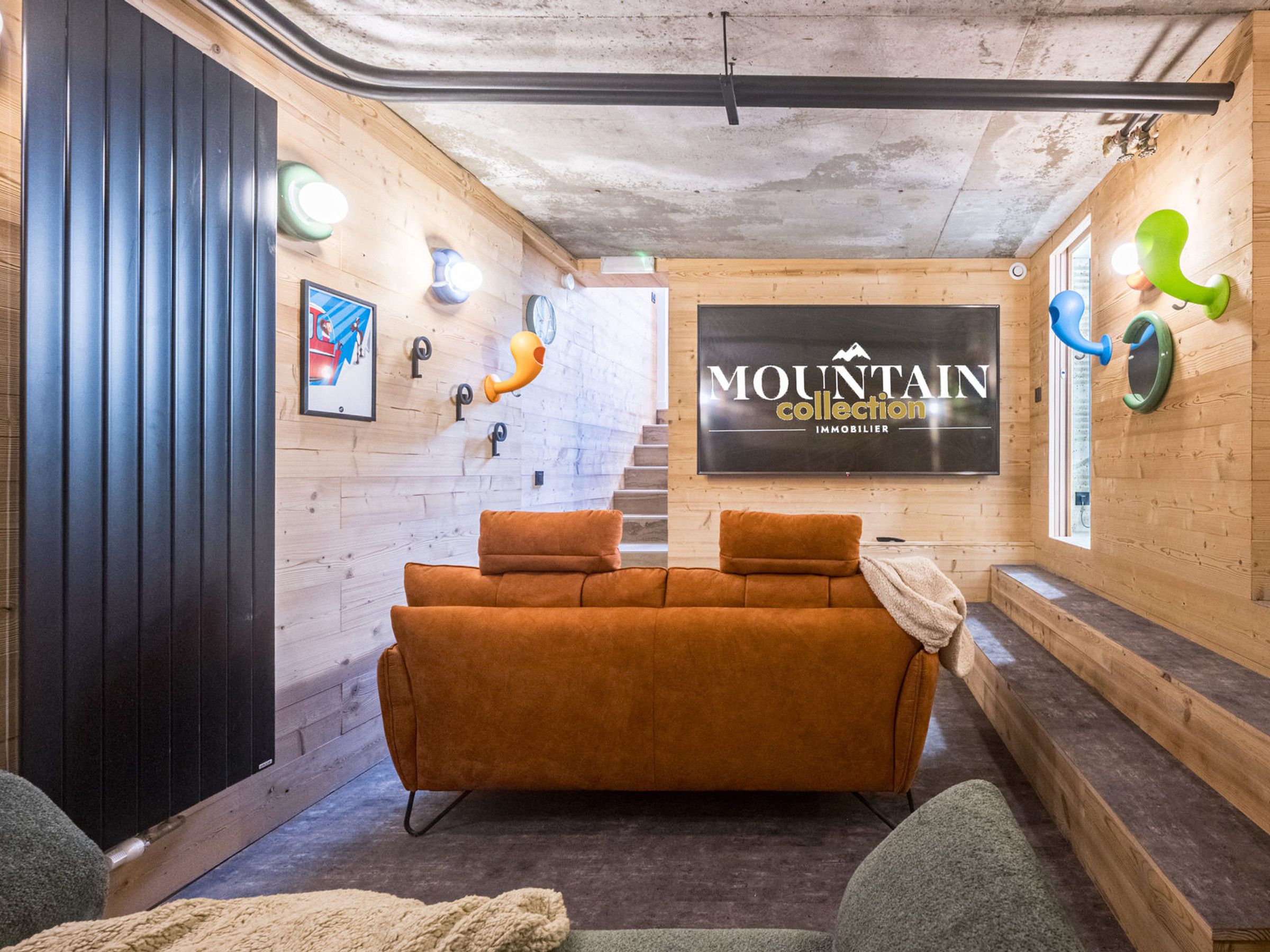A cozy interior with a sofa, a staircase, and a sign for 'MOUNTAIN collection IMMOBILIER'.