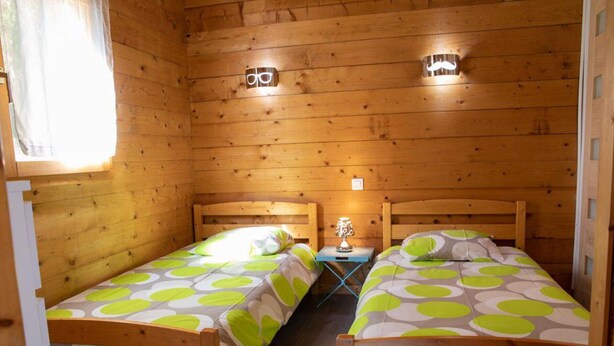 A cabin with two wooden beds, each with a headboard and a bedside table. - Cozy chalet in La Gazonne - 5 guests (Sauveterre-de-Rouergue)