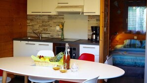 A compact kitchen with white cabinets, a stone backsplash, and a dining area with a table set for two. - Cozy chalet in La Gazonne - 5 guests (Sauveterre-de-Rouergue)