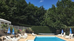A swimming pool with lounge chairs and umbrellas, surrounded by trees. - Cozy chalet in La Gazonne - 5 guests (Sauveterre-de-Rouergue)