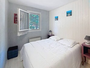 A bedroom with a bed, a window, a radiator, and a nightstand with a lamp. - Apartment with terrace - 5 guests (Merville-Franceville-Plage)