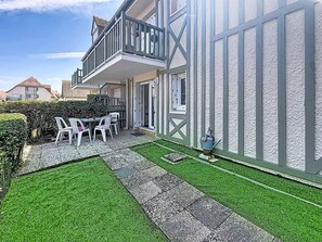 A residential property with a balcony, a small patio area with a table and chairs, and a well-maintained lawn. - Apartment with terrace - 5 guests (Merville-Franceville-Plage)