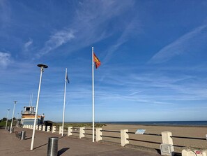 A coastal walkway with a lifeguard tower, a flagpole with a flag, and a clear view of the beach. - Apartment with terrace - 5 guests (Merville-Franceville-Plage)