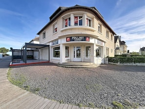 A two-story building with a ground-level entrance and a covered outdoor seating area. - Apartment with terrace - 5 guests (Merville-Franceville-Plage)