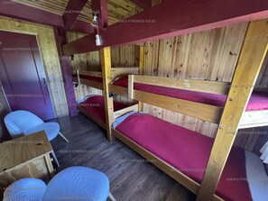 Ein Schlafzimmer mit Etagenbetten, Holzboden und -wänden, einer Tür und zwei Stühlen.