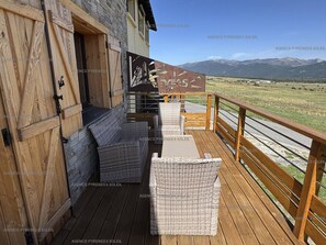 Eine Holzterrasse mit Korbmöbeln und Blick auf Berge.