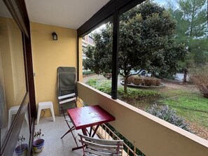 A balcony with a table and chairs, a small stool, and a potted plant. - Apartment with AC, private parking - 4 guests (Balaruc-les-Bains)