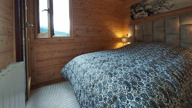 Ein Schlafzimmer mit Holzwänden, einem Bett mit gemustertem Überwurf, einem Nachttisch mit Lampe und einem Fenster mit Blick.