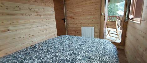 A bedroom with a bed, a radiator, and a sliding door leading to an outdoor area with a chair.