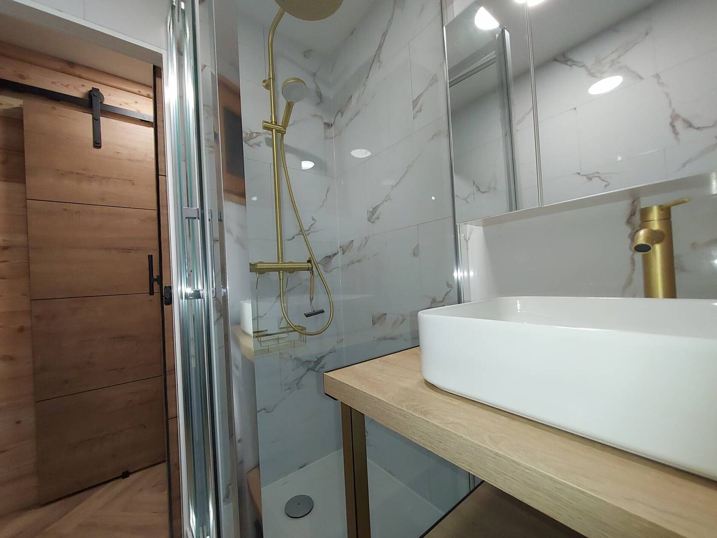A modern bathroom with a glass-enclosed shower, a white sink, and marble walls.