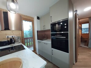A compact kitchen with a built-in oven, a coffee maker, and a view of the outdoors through a window. - Cozy apartment with panoramic view - 4 guests (Valmorel)